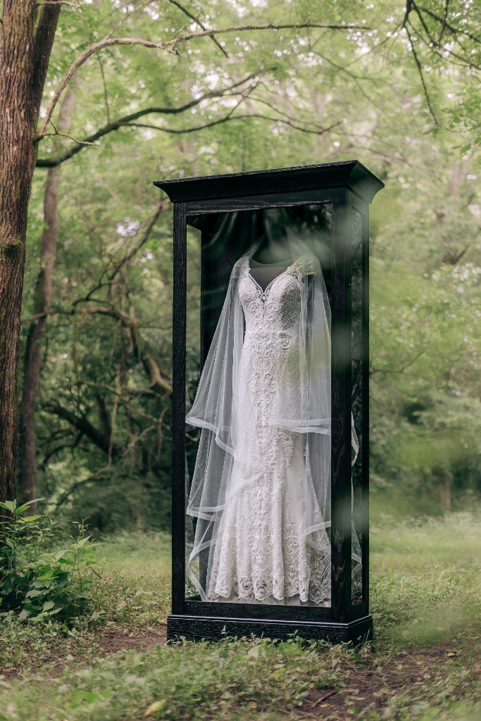 A freestanding Mrs. Case Signature displaying a lace gown and veil in a green wood
